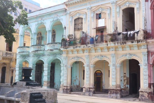 Elegant but run down colonial buildings along the Prado Avenue in Havana in light blue, light yellow and pink painted colors with elaborate details on the windows, doors and balconies.