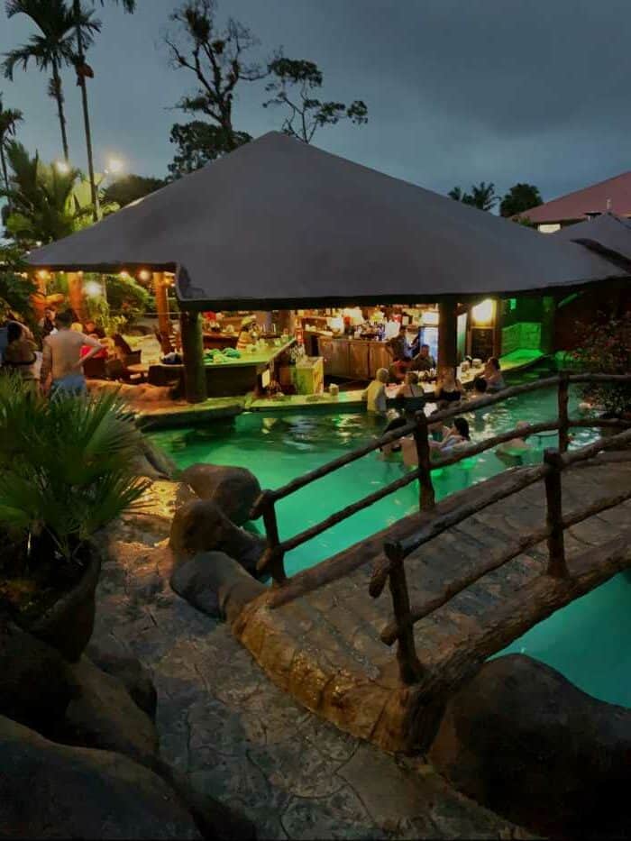 Arenal hot springs in Costa Rica, beautifully lit at night, with green water pools, bars, and bridges. 