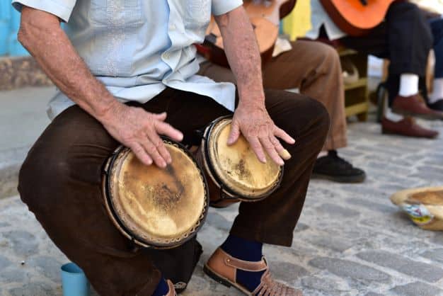 A man seated playing two small drums with his hands at the same time
