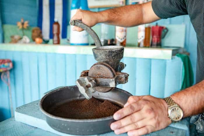 A man grinding coffee beans with an old fashioned coffee grinder in a blue kitchen
