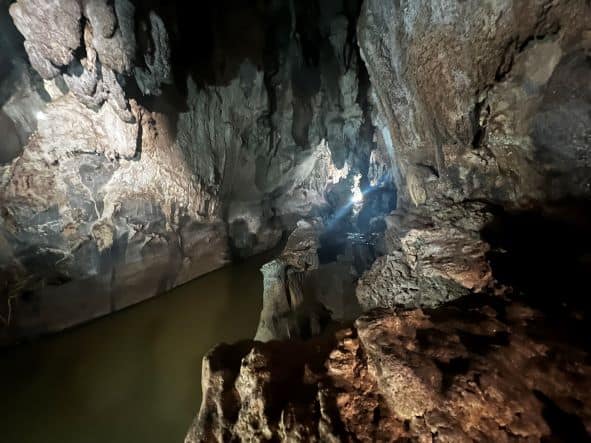 Inside the Cueva del Indio in Vinales with rugged stone walls and ceiling, and an underground river lit by artificial lighting