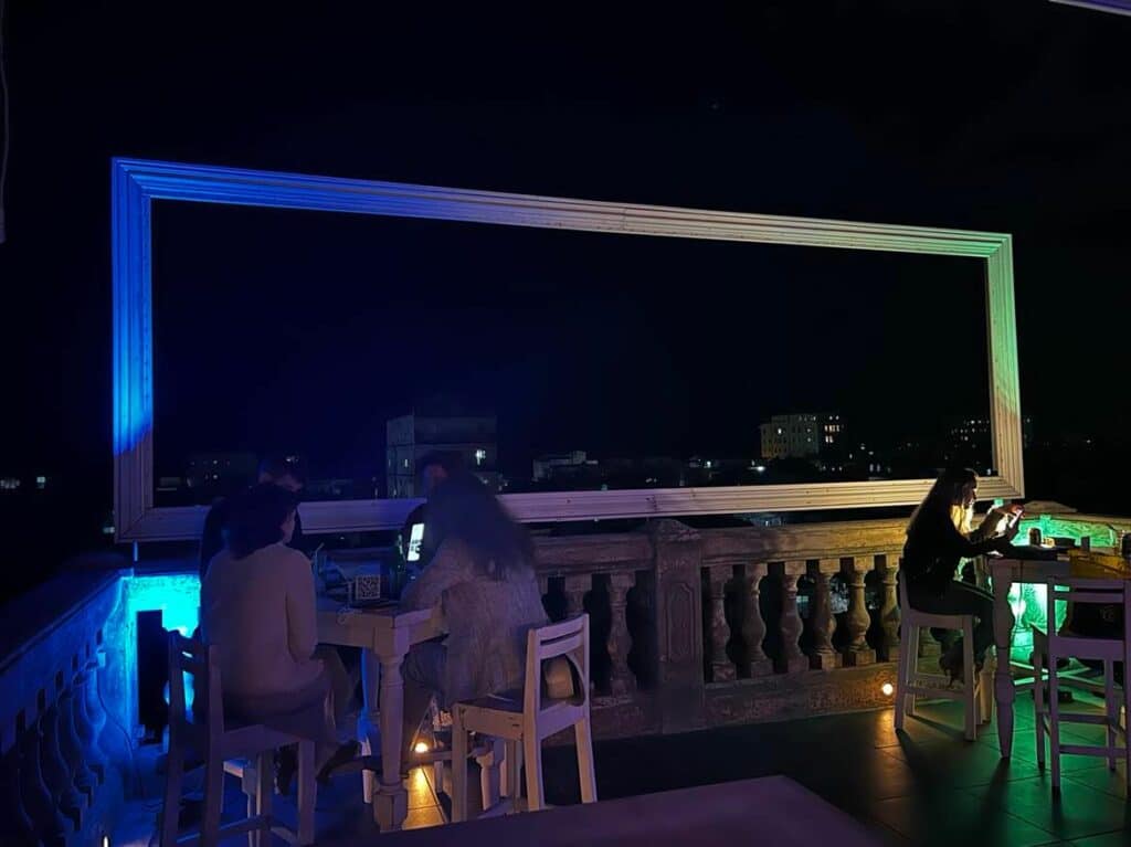 Night at the La Guarida rooftop bar in Havana, people seated with a drink in the sparingly lit terrace with incredible views of Havana outside the fence