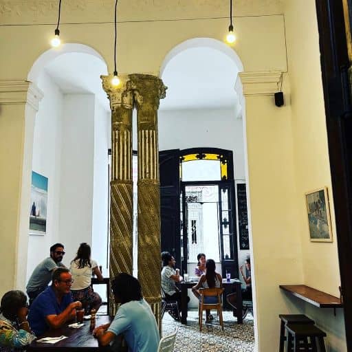 Paladar El Cafe in Old Havana with elegant interior of columns, white walls and high ceilings. The rooms are divided by archways, and you can see through the doorway to the street outside. 