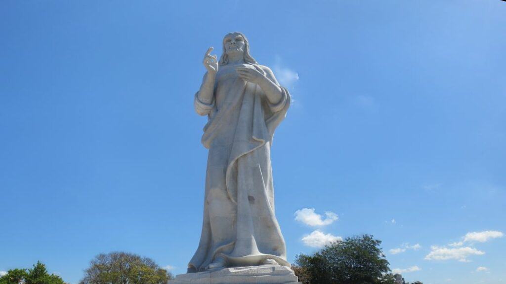 The huge, white statue of Christ on the other side of the Havana Harbor on a bright summer day under a blue sky. 