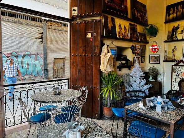 The eclectic interior with a myriad of details and decorations in Paladar El Dandy in Old Havana. Tables with artsy chairs, plants, photos, and the large wooden window shutters are open to the street life outside. 