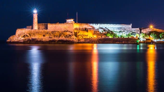 El Morro lighthouse at night across the Havana Bay bathed in warm lights against the dark water