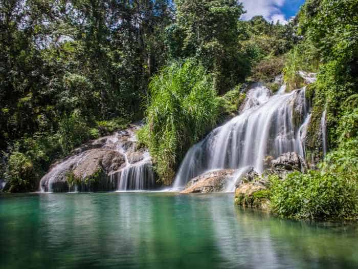 The beautiful El Nicho waterfall in a Cuban National Park, the white water puring down into a green beautiful lake amidst green trees and bushes