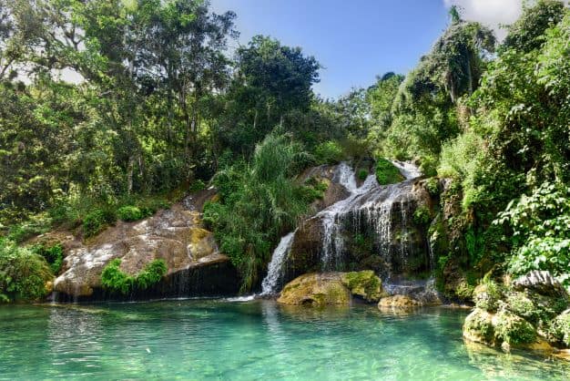El Nicho waterfall running into crystal clear greenish water, surrounded by lush green bushes and trees
