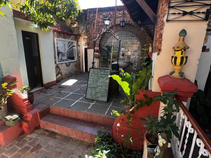 A ccharming cafe in Trinidad Cuba, with red tile stairs to the elaborately decorated entrance area, with maroon bricks, photos, and artsy details side by side with green plants. 