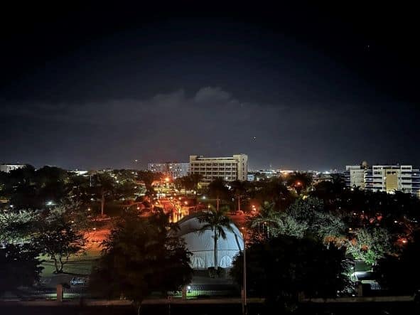 Emancipation Park in Kingston at night, you can barely see the trees lit from behind, and the street lights and buildings in the background