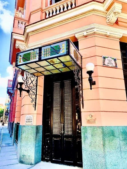 The beautiful corner entrance to the Hotel Ambos Mundos, with beautiful decorations, pink and green walls on both sides, and elegant lamps. 