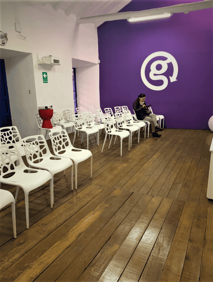 Meeting at the G Adventure HQ in Cusco. White chairs for all the trekkers, and only one woman seated at the moment. The far wall is deep purple. 