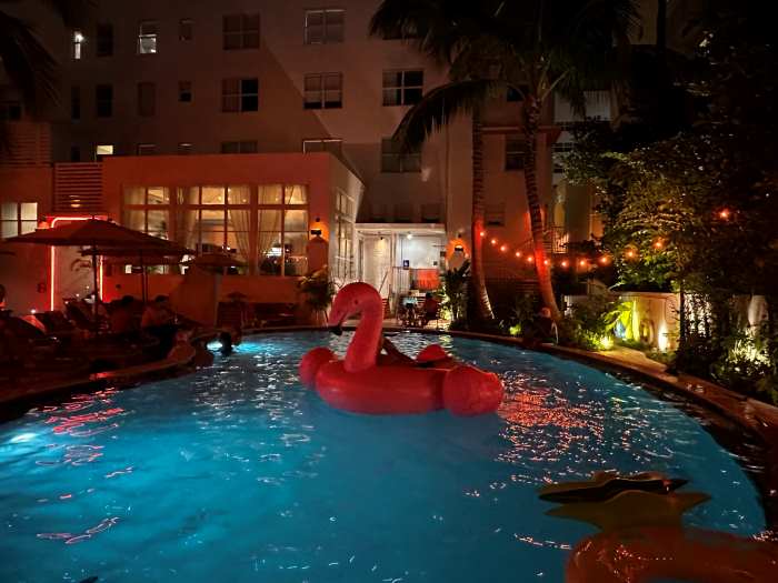 The backyard pool at the Generator Miami Beach at night, with warm lights, blue pool, and a huge pink plastic flamingo floating in the pool
