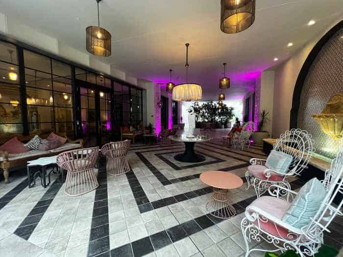 The entrance to the Goodtimes Hotel from Washington Avenue, with black and white tiled floors, elegant elaborate white chairs, and purple neon lighting by the glass walls and entrance. 