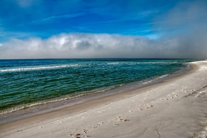 Grayton Beach State Park, with light sand against the greenish water on a sunny day that has clouds in the distance in the sky