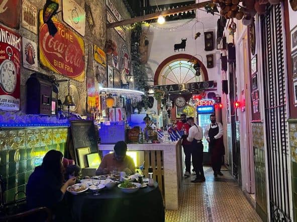 Colorful interior at Paladar San Cristobal in Central Havana, waiters working, lots of light, ornaments, photos and art everywhere. People seated at the tables enjoying their dinner. 