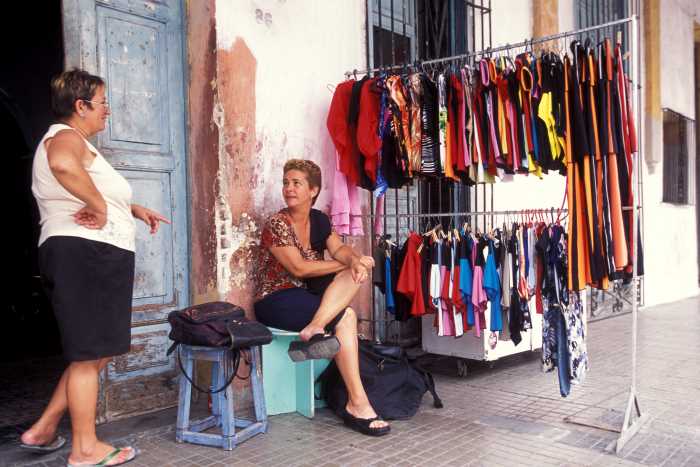 A variety of a ventanita in Cuba, a lady sitting outside her home with a rack of clothes for sale