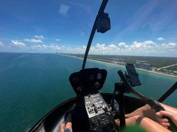 The vast view from the glass cockpit of the green water underneath, and the thin strip of white sand along the coast under the blue sky