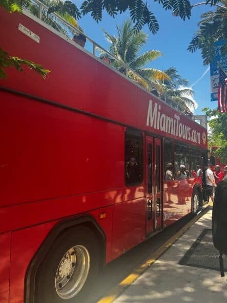 The red hop on hop off bus in Miami, on a bright sunny summer day surrounded by palm trees, people, and above is a blue sky