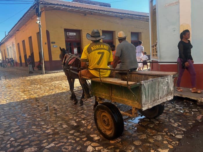 A man driving a horse and old fashioned wooden carriage along the cobblestoned streets of colonial town Trinidad in Cuba