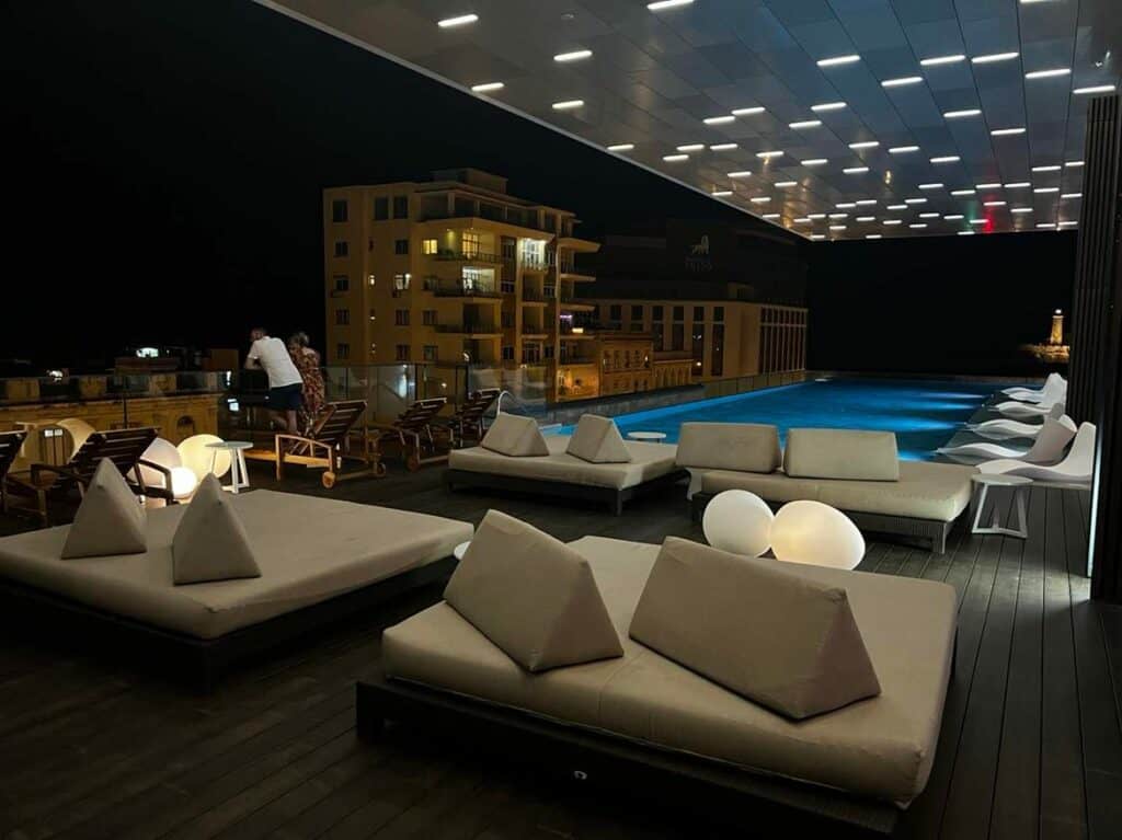 The pool floor at Grand Packard at night, with elegant white seating areas, the blue pool lit in the background, and you see the El Morro lighthouse in the distance across the Havana Bay. 