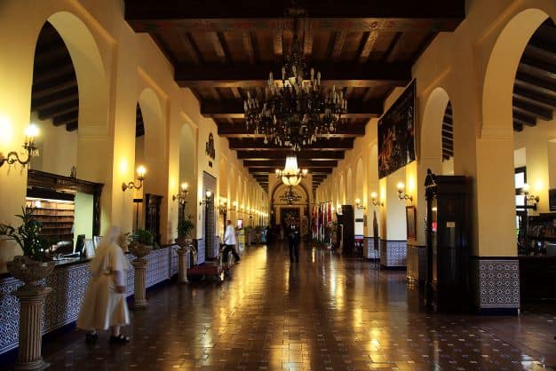 The vast, elegant foyer at Hotel Nacional de Cuba with artwork, dark high wooden ceilings, archways, and a blank stone floor with golden lighting