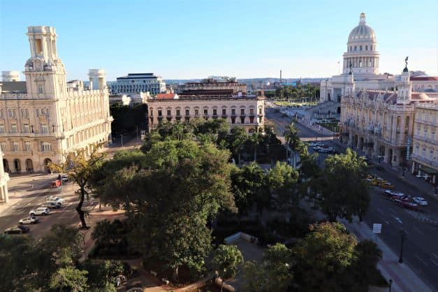 Overview photo of Parque Central in Havana, filled with big trees an surrounded by large eleganti colonial buildings like the Grand Theater, the Capitolio, and the Museum of Fine Arts on a sunny day. 
