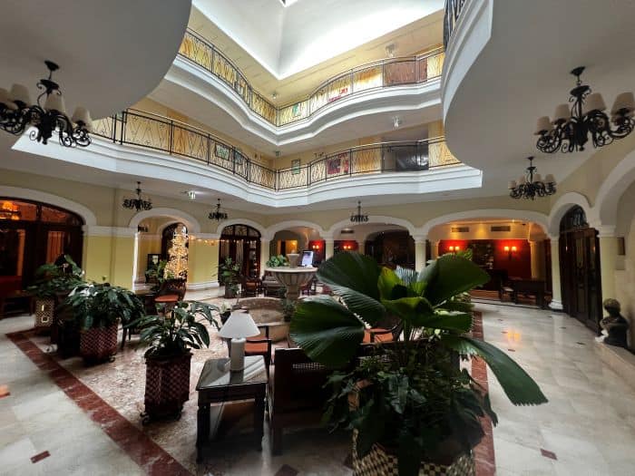 The airy elegant foyer in the Iberostar Hotel in Trinidad, with white marble floors, lots of green plants, an open ceiling where you see the walkways around the second and third floor, and light coming down from above