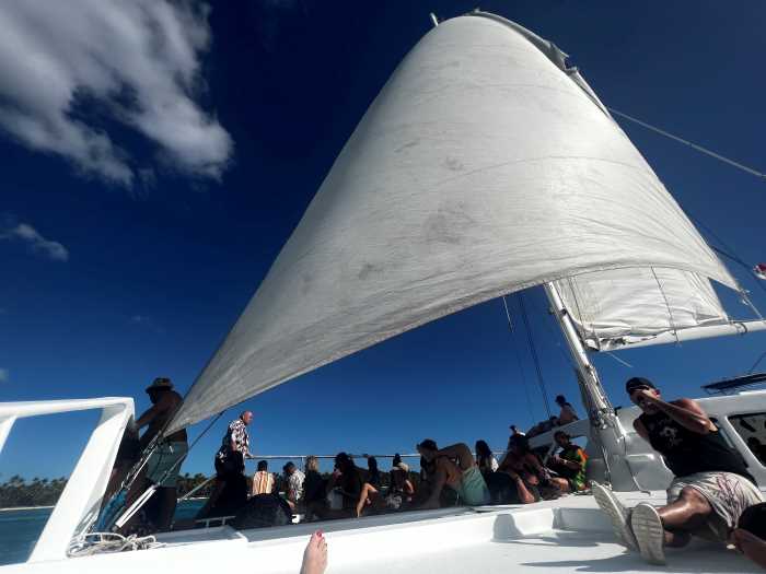 Day trip from Punta Cana in a beautiful white sail boat, the white sail full against the blue sky above and people relaxing on deck. 