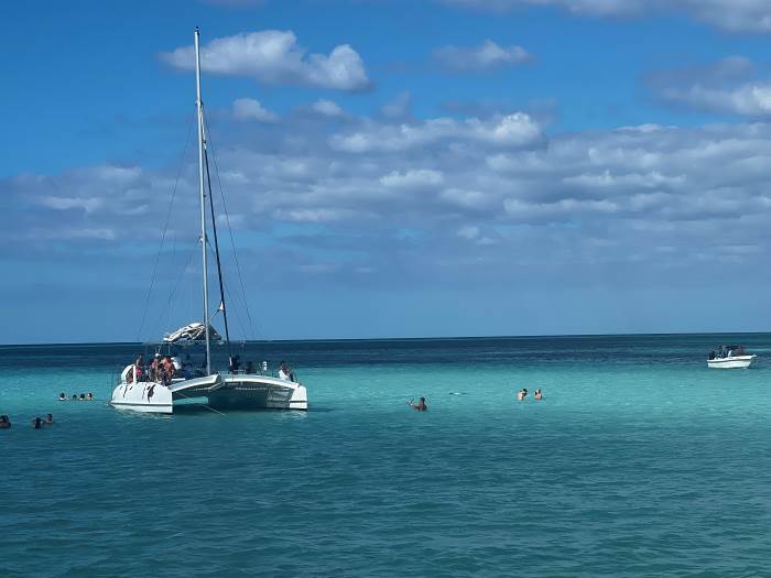 Catamaran tour in the Dominican Republic; a white beautiful catamaran on the greenish blue water, people snorkeling around the boat under the blue sky with white dots of clouds