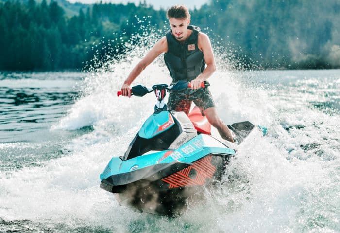 A man in full speed ahead on a jet ski on the water, the sea splashing around him, as he is standing on the jet ski steering in the waves