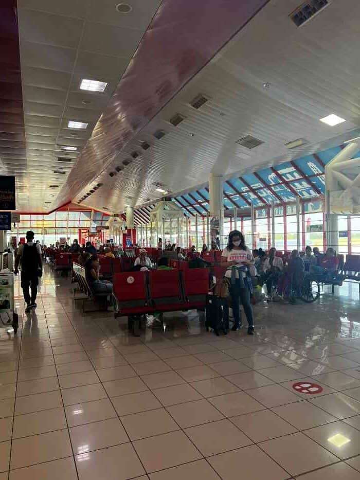 The departure hall at Jose Marti International Airport in Havana, with white tiled floors, a high ceiling, and red seating, with lots of people. 
