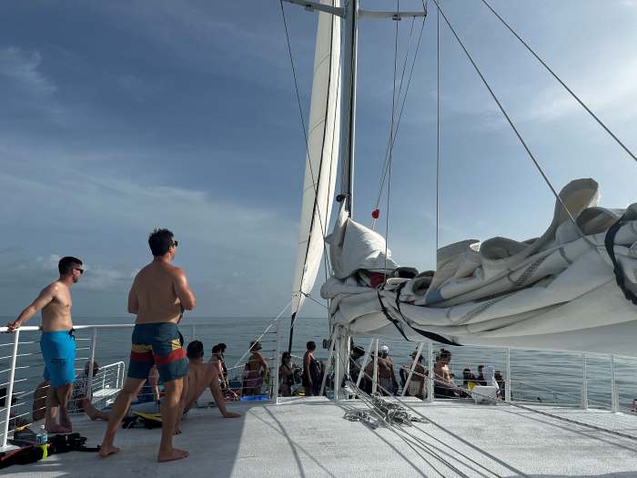 From a catamaran cruise outside Key West on a bright white elegant catamaran, the sails olded, the deck white and people enjoying the sunny day. 