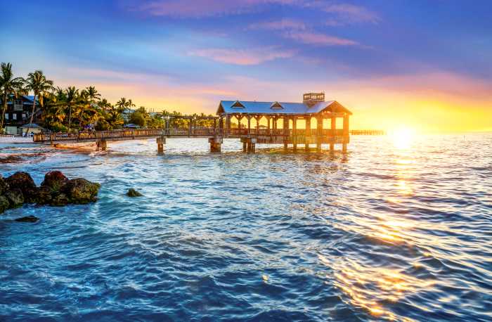 Key West pier in the sunset, with the golden sun in the distance reflecting in the water behind an overwater cottage