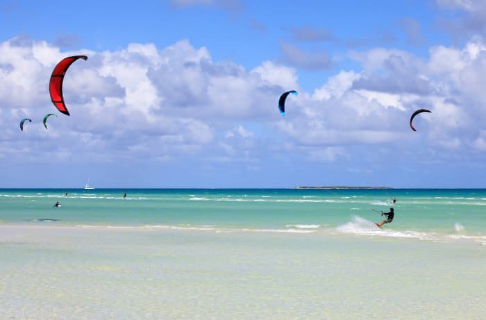 Lots of people kite surfing in Cayo Guillermo in Cuba, on crystal clear calm water, on a bright sunny summer day with blue skies and a few white clouds in the distance. 
