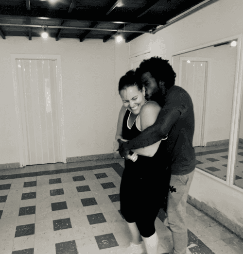 Black and white photo of Kizomba teachers and couple Tony and Loliett in Havana Cuba. He is holding around her kissing her cheek, and she is smiling wide! 