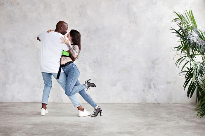 Man and woman dancing the Kizomba,  in the middle of a figure where he pulls here close tilting her over so she stands on one leg, leaning towards her partner. 