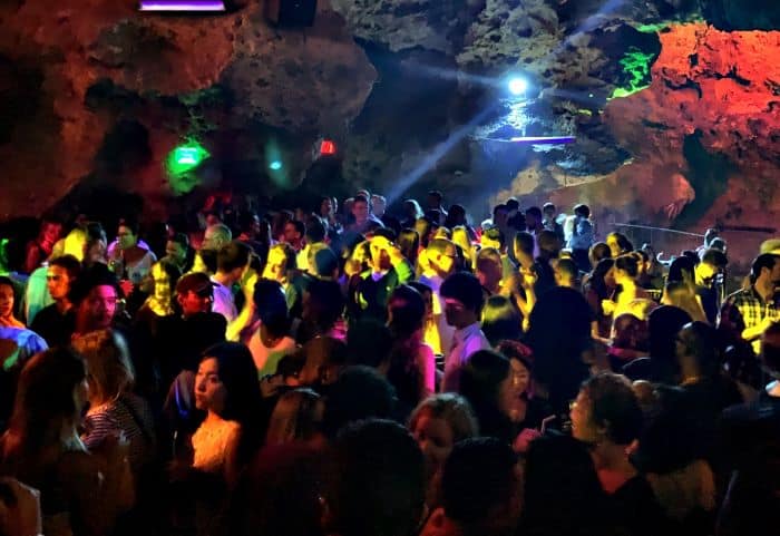The packed dance floor in Disco Ayala, La Cueva night club in Trinidad, Cuba. The dancing people are lit by colored lighting amidst the cave walls. 