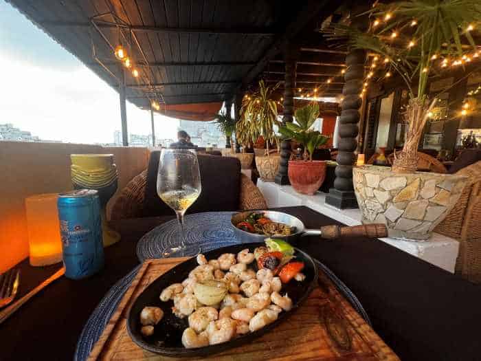 A shrimp meal and glass of white wine on an elegant table at La Terraza paladar along the Prado in Havana. The outdoor seating is on the second floor, and the restaurant area is inviting, with plants, lights, and warm colors of the interior. 