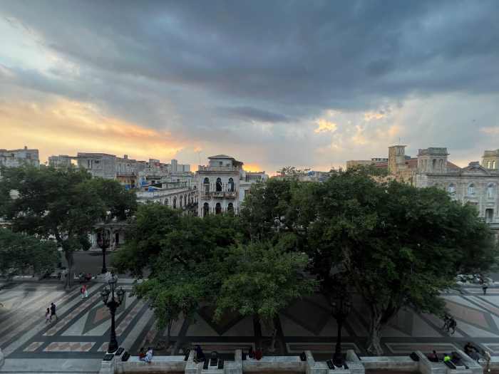 View of the Prado Avenue at sunset from La Terraza restaurant outdoor seating. Big trees in front of the city colonial buildings stretching to the back of the photo. 