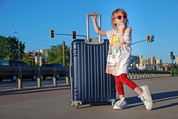 A little girl with a large suitcase beside a busy road