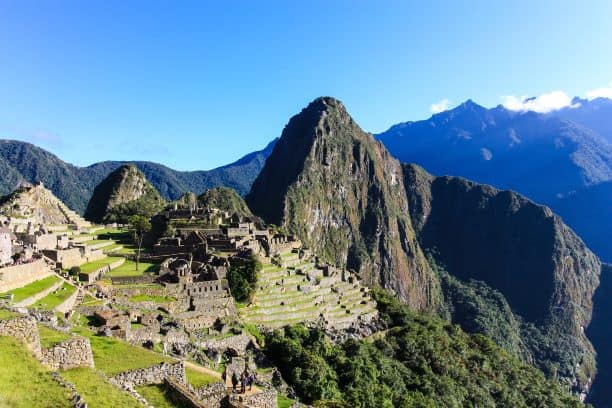 Arriving at Machu Picchu on a sunny morning, with the impressive ruins on a mountain plain with the steep peaks in the background, and vast mountain ranges behind the peaks again. 