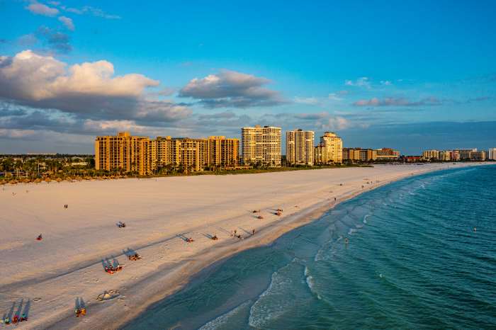 A beautiful photo of Marco Island wide beach around sunset when the shadeow of the few people on the white sands are long, and white highrises glowing from the setting sun in the distance