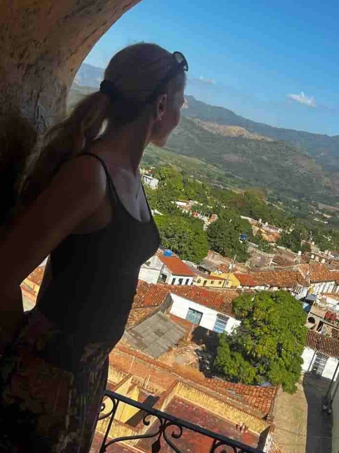 Me in an open archway on the top of the bell tower in Trinidad, where there is a vast view of Trinidad city, with old colonial houses, streets, and terracotta roofs in the sunlight