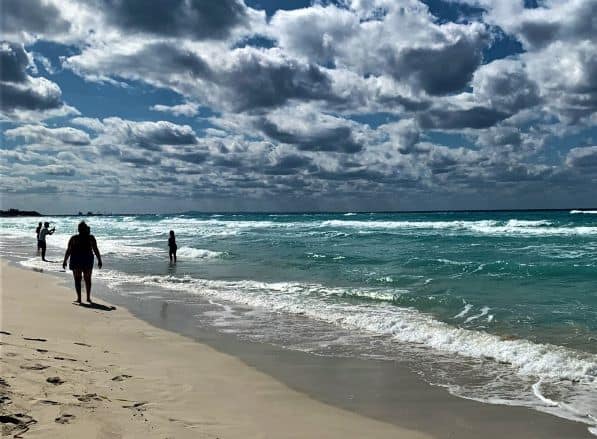 The light sands at Varadero beach on a sunny summer day, with crystal clear waters under the sky dotted with white clouds, people enjoying the water. 