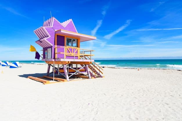 Miami is famous for its white sandy beaches and iconic colorful lifeguard stations, like this bright pink one on the white sands on a bright sunny day with blue skies