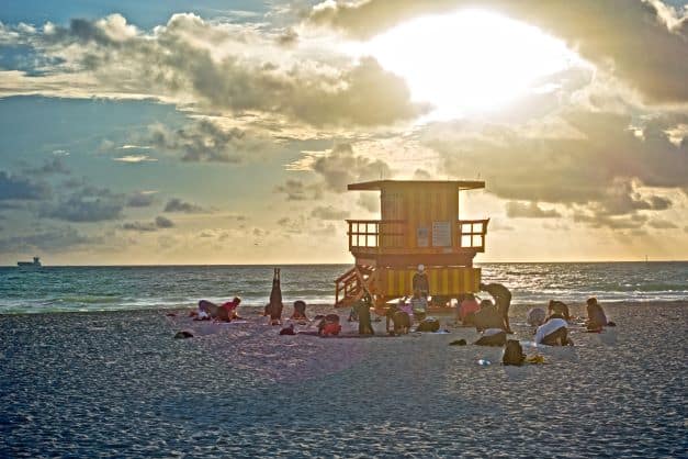 Morning yoga on the beach by a lifeguard station in Miami, the sky in a golden light from the rising sun