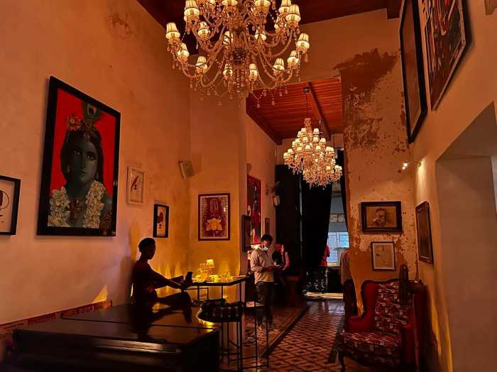 The elegant entrance to Paladar Mischifu in Central Havana, with warm lighting, art on the wihte walls, chesterfield furniture and impressive chandeliers. 