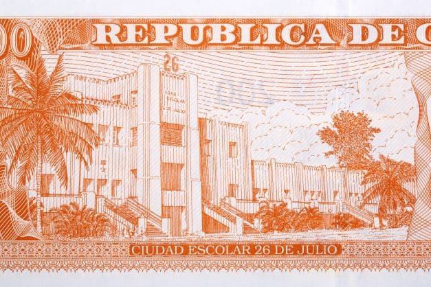 A Cuban pesos note with a drawing of the Moneda Barracks in Santiago de Cuba, in orange shades. 
