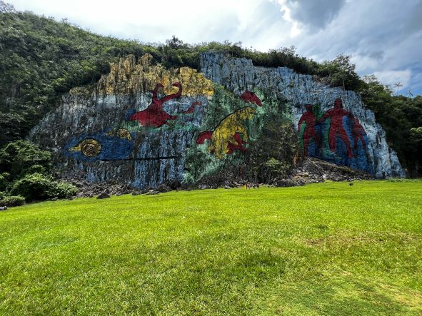 The mural that is painted directly on the mountain side in Vinales Valley Cuba: Mural de la Prehistoria. A huge mural painted in the 60s, with a large green grass field in front